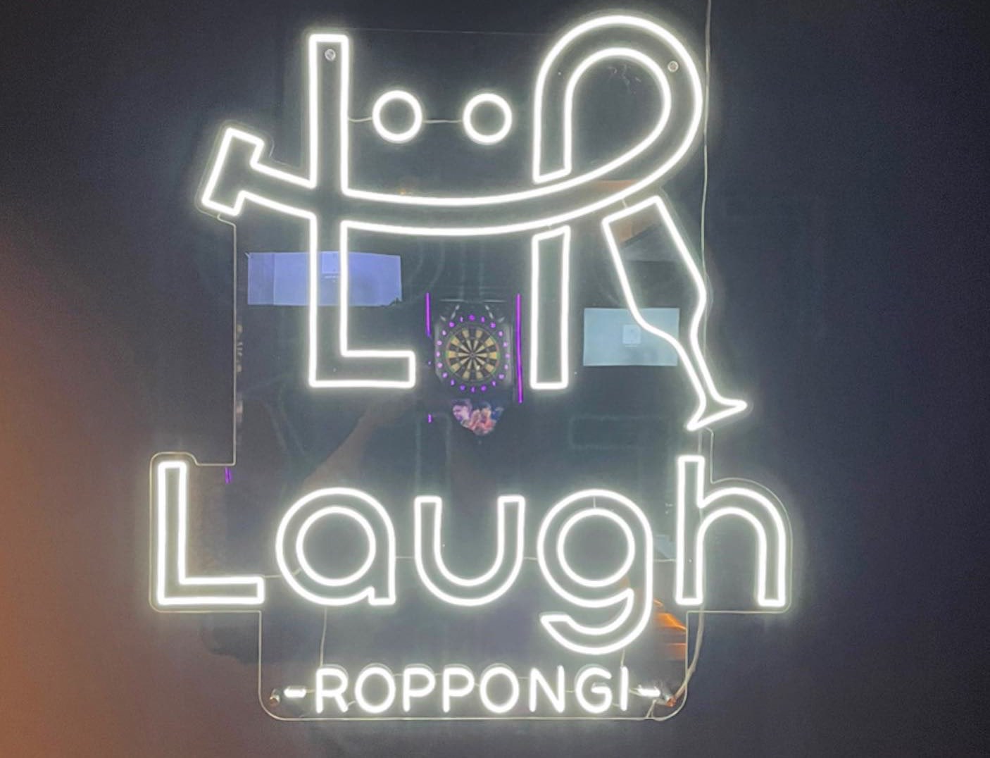 暗い壁に白く光るネオンサイン。ロゴマークと「Laugh -ROPPONGI-」の文字。